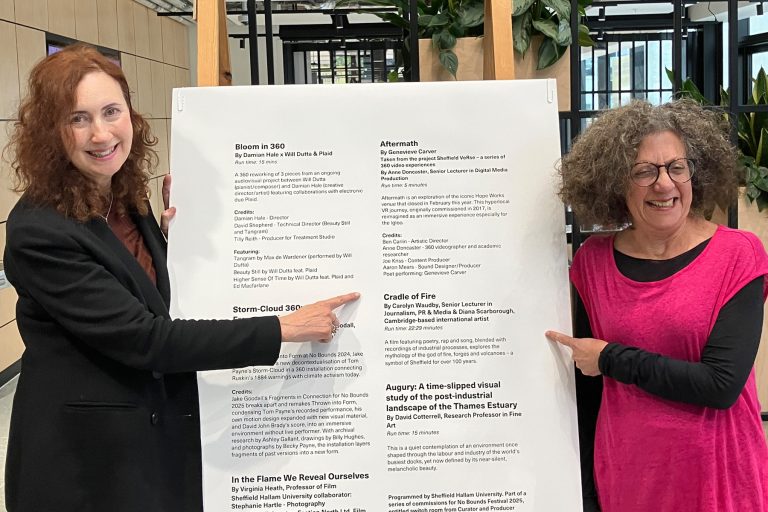 Carolyn Waudby wearing black and Diana Scarborough wearing pink paint at a large white notice board showing igloo festival programme for No Bounds Festival 2025 - D. Scarborough©