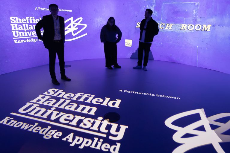 360 degree projection screen space with 3 people. Coloured purple background with white text on walls and floor- Sheffield Hallum University