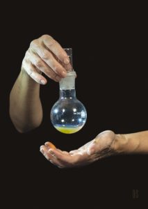 one hand holding chesty flask of gold and silver liquid