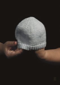 two hands holding a light blue baby hat