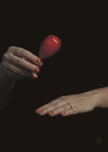 one hand shaking a small red baby rattle, other hand is resting