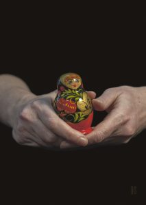 two hands holding a small wooden painted Russian doll
